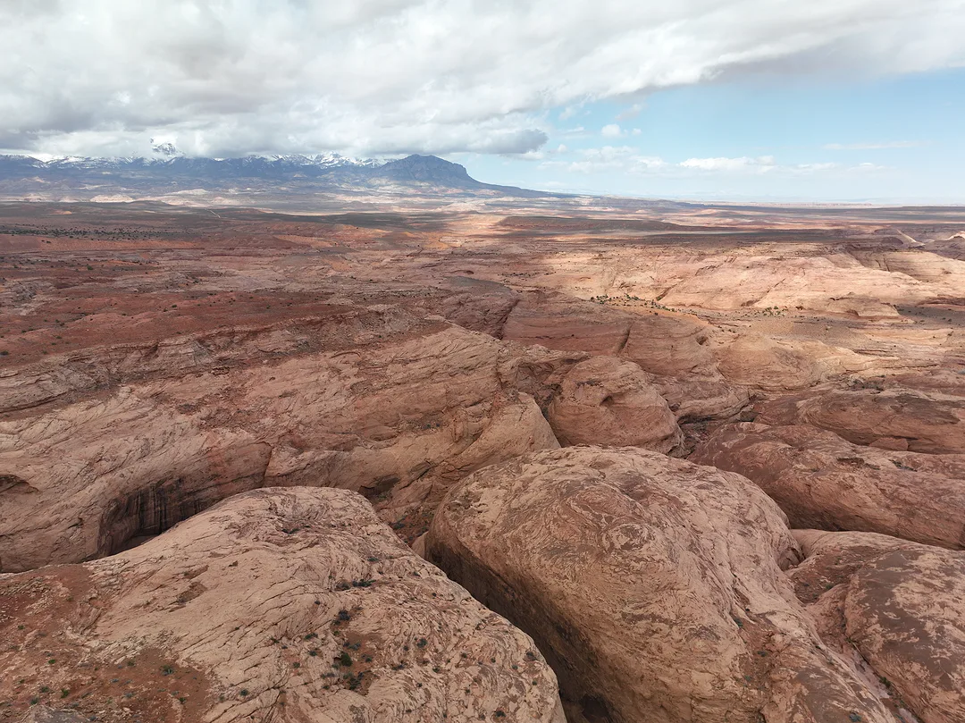 Pale slickrock canyons folding away toward a distant mesa, storm cloud over the mountains beyond