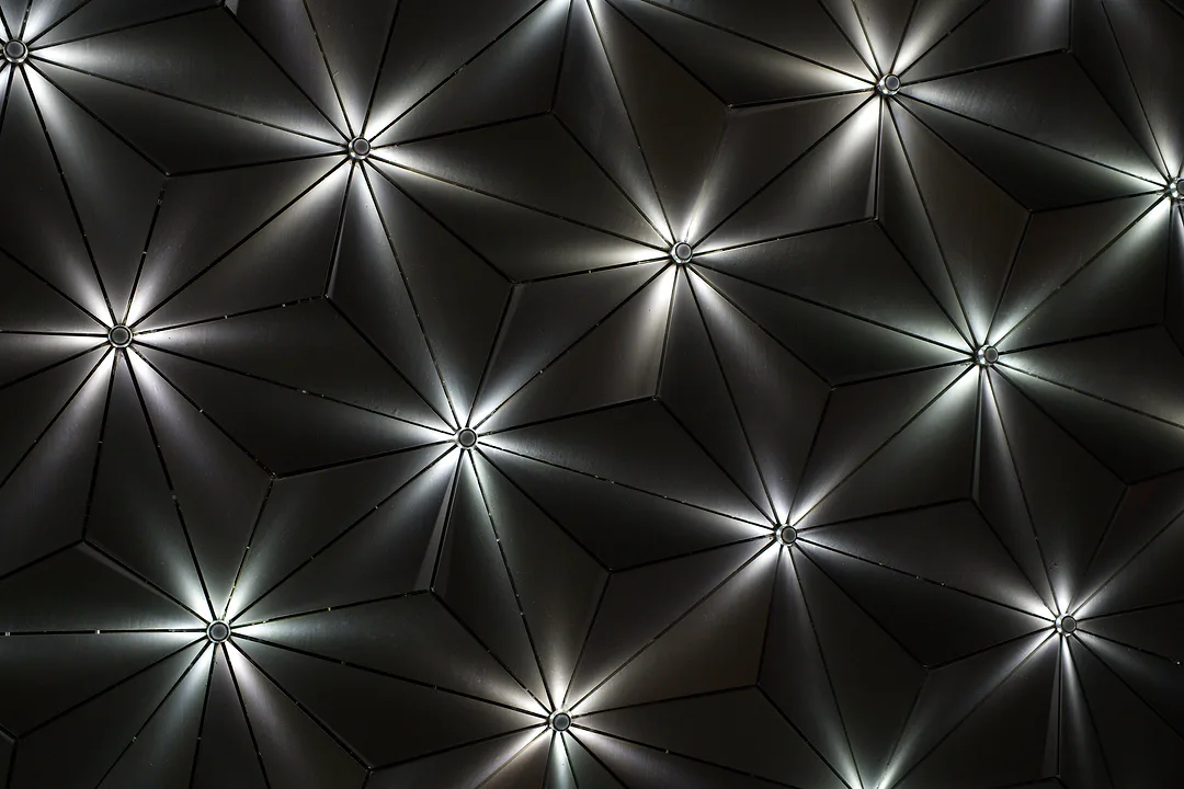 Close view of a dark geometric ceiling, starbursts of light spreading from the centre of every panel