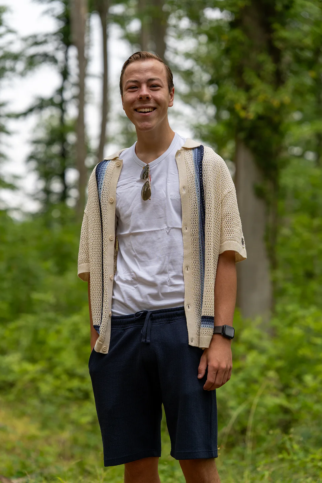 Young man laughing on a forest path, one hand in the pocket of his navy shorts