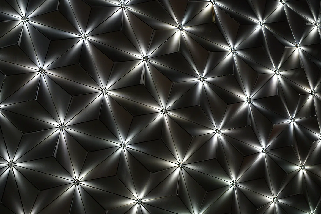 Ceiling of dark faceted panels, light radiating in spokes from a point at the centre of each triangle