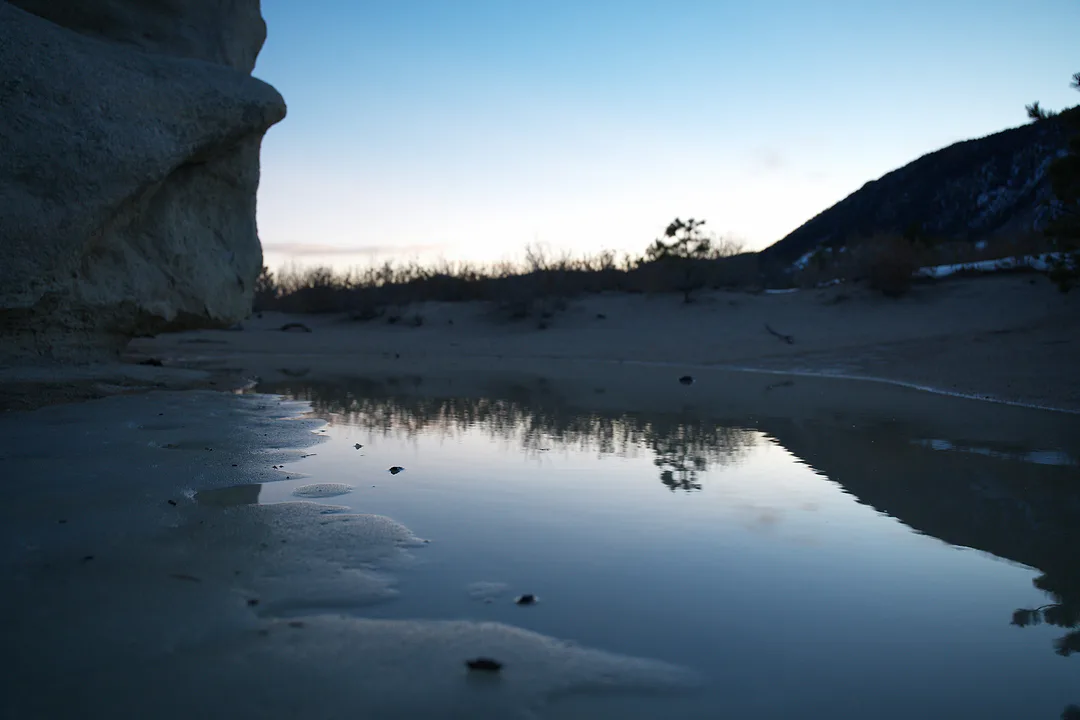 Still water at dusk reflecting the pale sky, a sandstone bluff on one side and a dark hill on the other